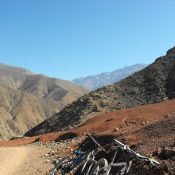 A scenic view of rugged Atlas Mountains with parked mountain bikes on a dirt trail, under a clear blue sky.