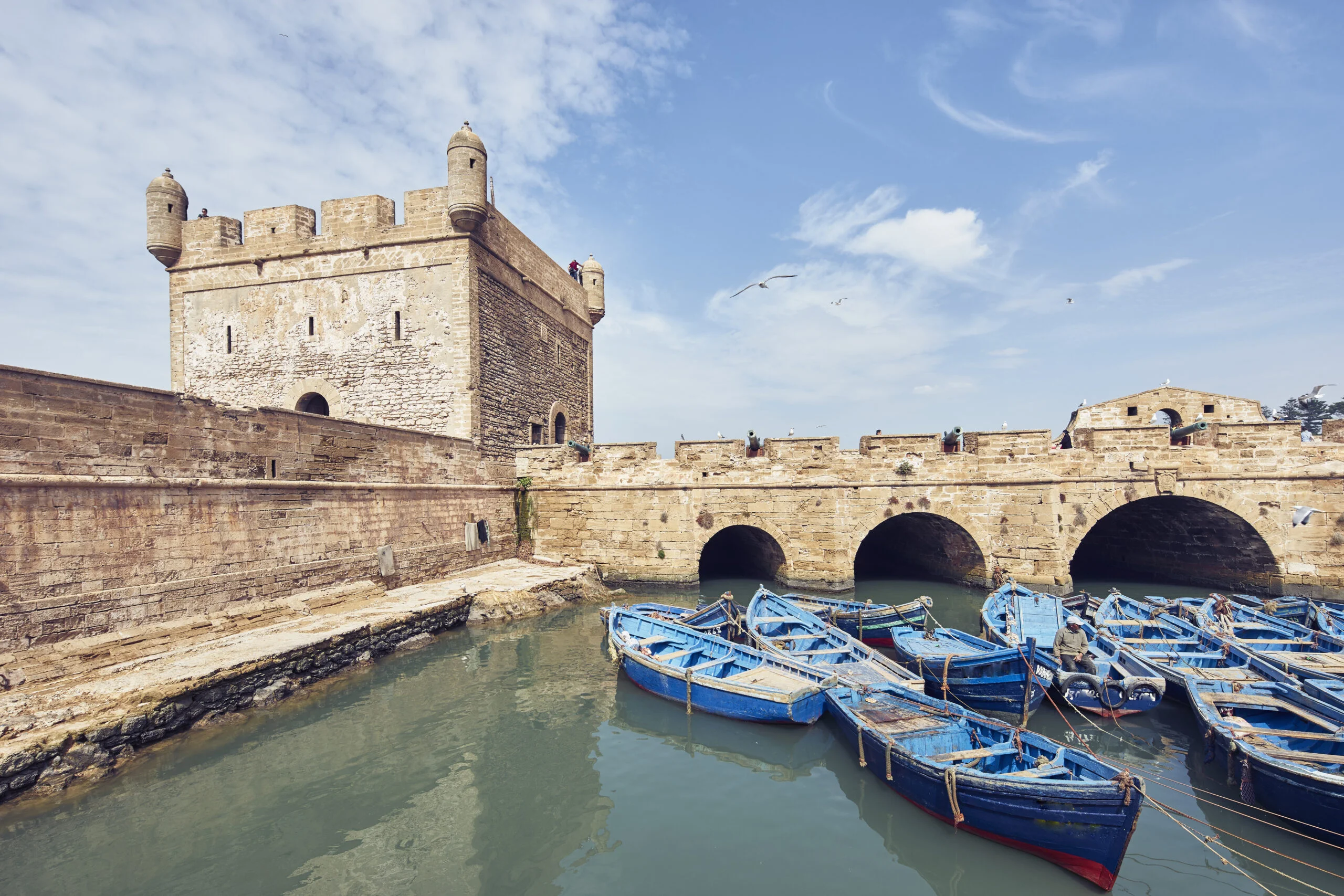 Blue boats floating by an ancient fortress under a clear sky.